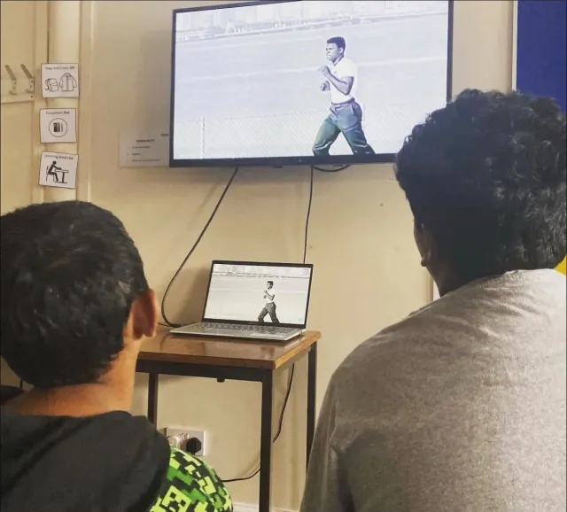 Two children watching a film about Muhammad Ali on a TV screen