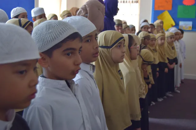 Children in white caps and gold headscarves standing in rows at an assembly
